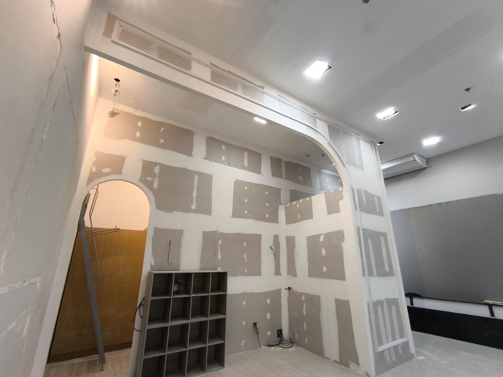 Arco curvo em drywall com parede em boiserie e nichos embutidos, em obra comercial executada pela JL Drywall