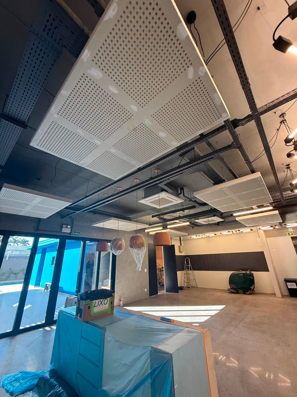 Forro modular acústico perfurado instalado em obra comercial, com estrutura e dutos aparentes